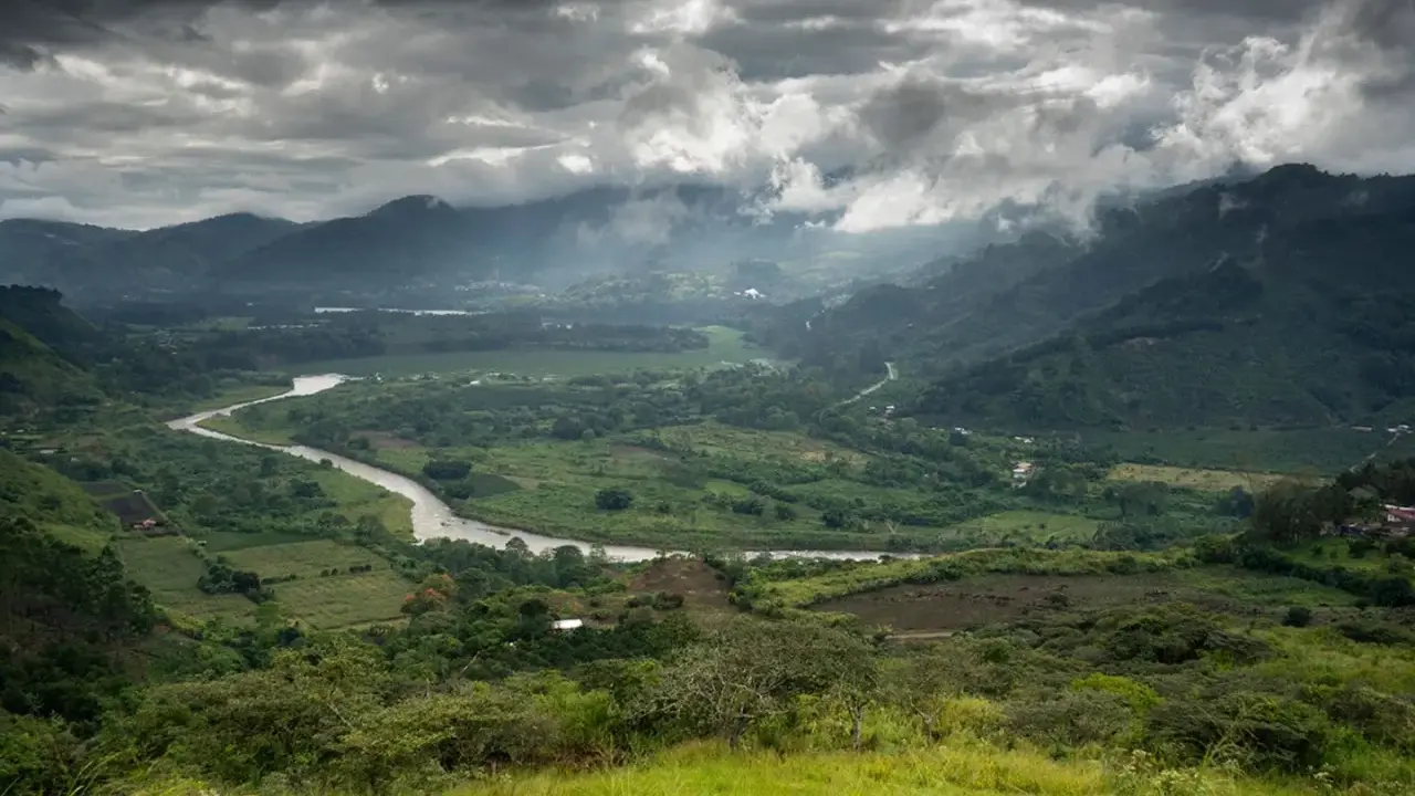 Ein gewundener Fluss schlängelt sich durch ein grünes Tal in Costa Rica. Wolken ziehen über die Berge, die das Bild umrahmen.