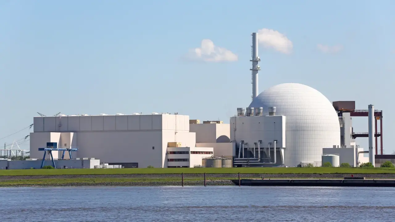 Großes Kernkraftwerk mit Kuppel und Kühlturm am Wasser.