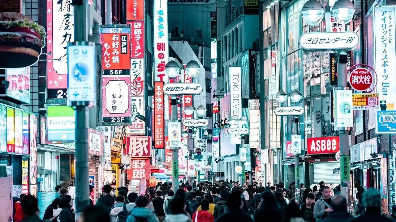 Eine belebte Straße mit vielen leuchtenden Neonschildern, die Geschäfte und Restaurants bewerben. Dies ist ein typisches Beispiel für einen urbanen Raum, voller Leben und Aktivität.