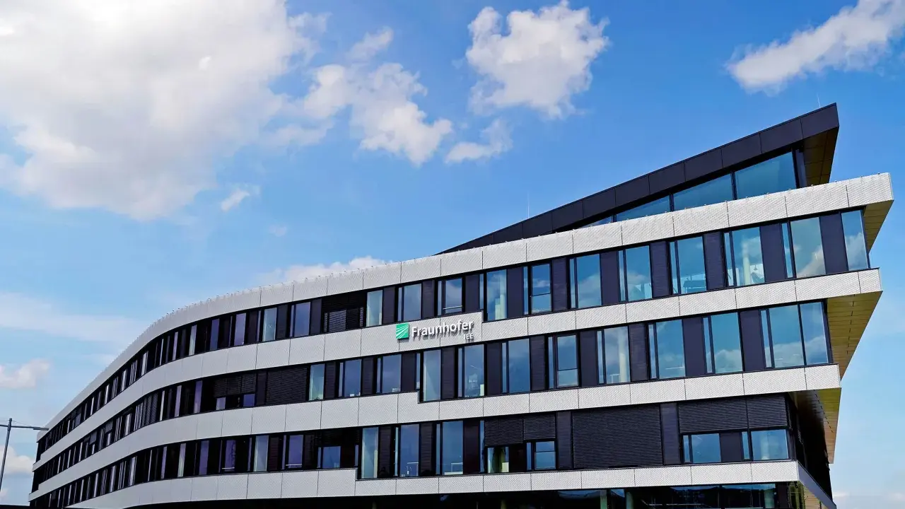 Modernes Gebäude des Fraunhofer IEE mit geschwungener Fassade und vielen Fenstern unter blauem Himmel mit Wolken.