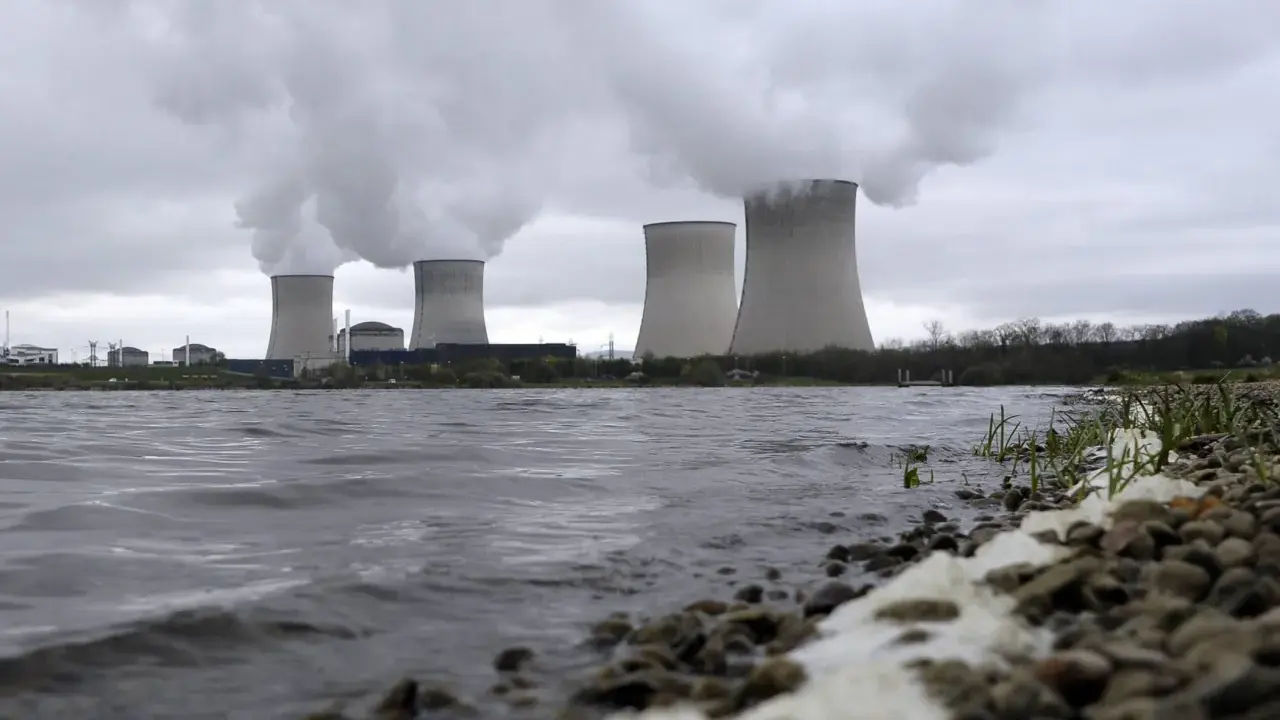 Kühltürme eines Atomkraftwerks mit Dampfschwaden über einem Flussufer.