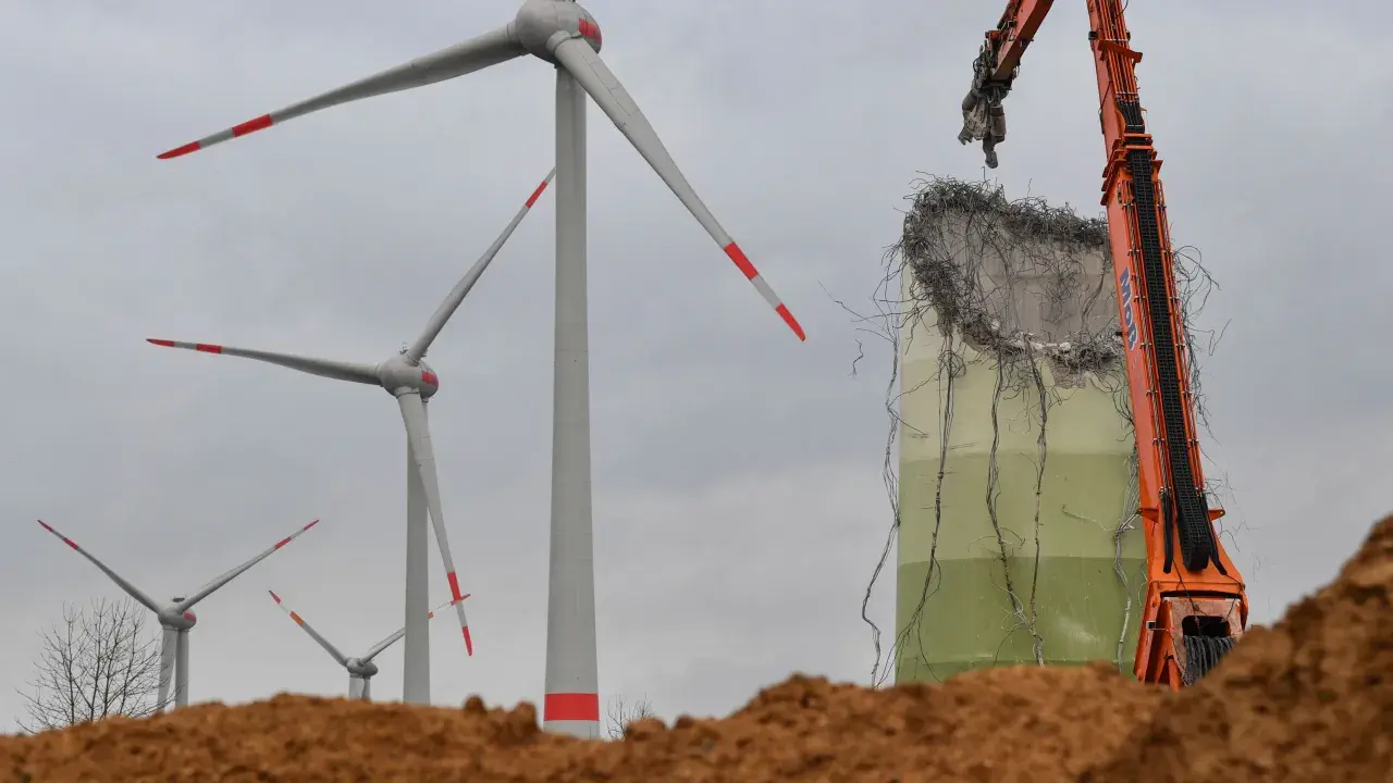 Abrissbagger demontiert eine Windkraftanlage. Im Hintergrund stehen noch weitere Windräder, die ihre lange Laufzeit hinter sich haben.