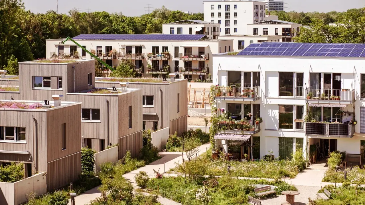 Moderne Gebäude mit Gründächern und Solaranlagen, umgeben von üppiger Vegetation. Ein Beispiel für nachhaltige Quartiersentwicklung.