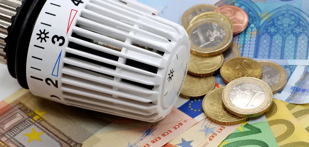 Thermostat mit Euro-Münzen und Scheinen. Heizkosten steigen, CO2-Geld wird knapp.