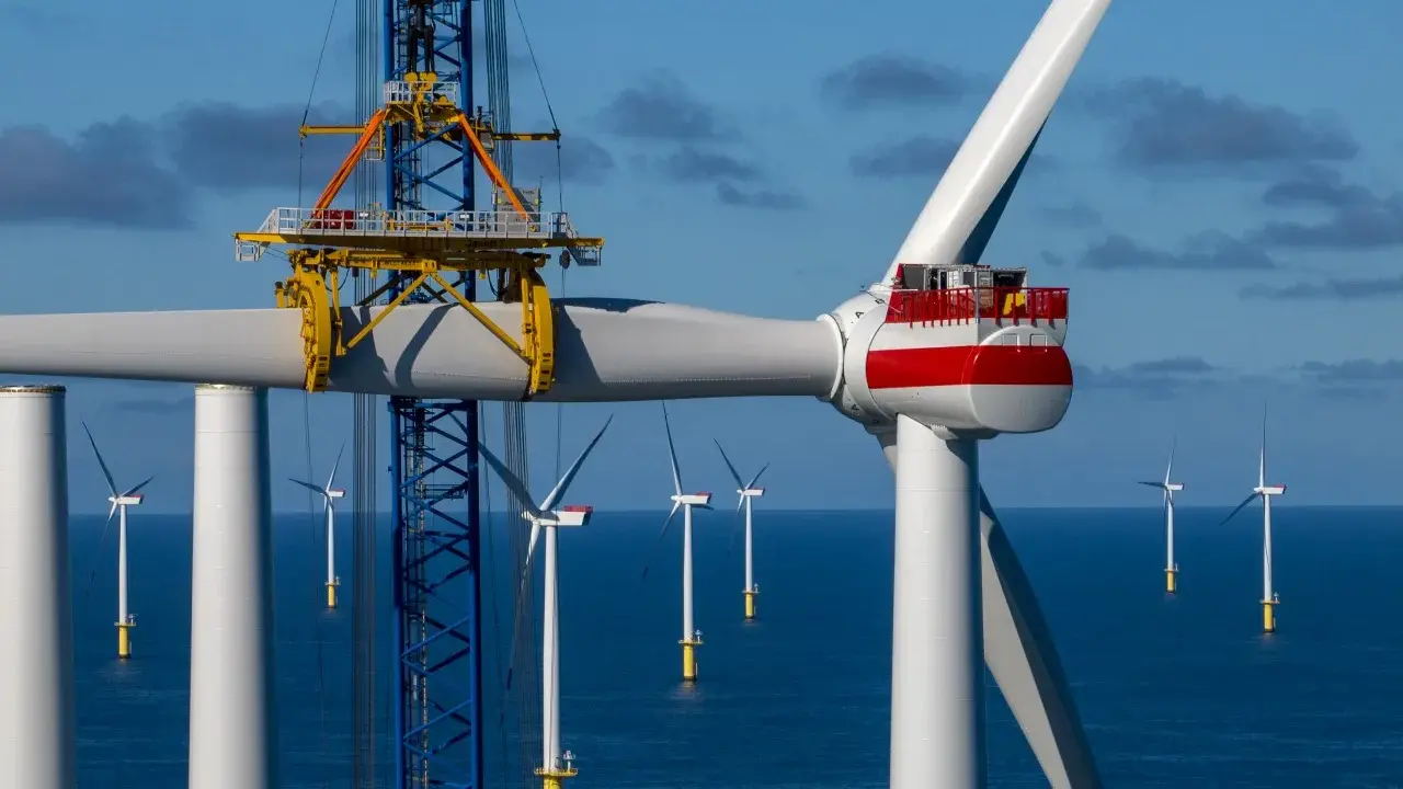 Bau eines Offshore-Windparks für die **Energie Niederlande**. Ein Kran hebt ein Rotorblatt einer riesigen Windkraftanlage im Meer.