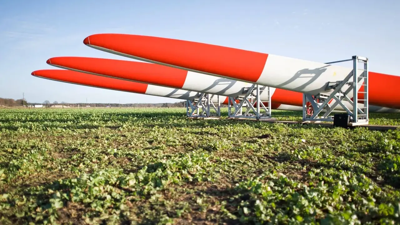 Drei Rotorblätter für Windkraftanlagen liegen auf einem Feld. Sie sind rot-weiß gestreift und warten auf ihren Einsatz nach dem EEG.