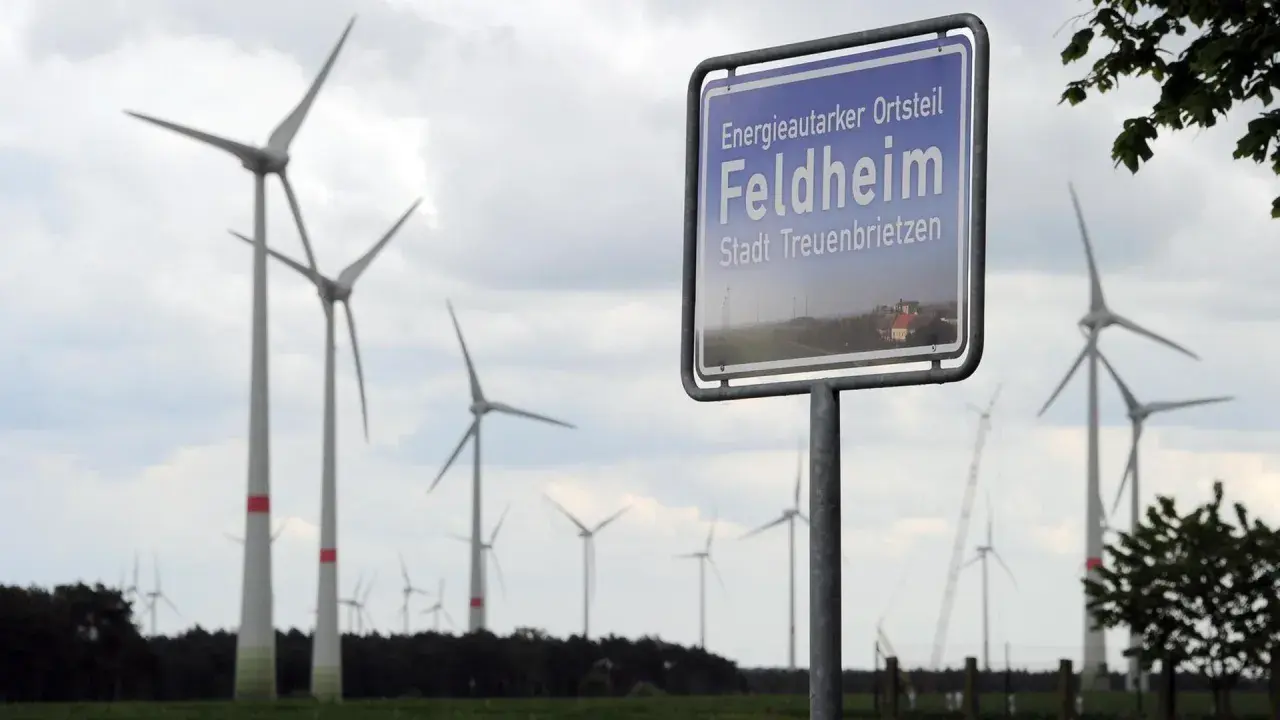 Schild "Energieautarker Ortsteil Feldheim, Stadt Treuenbrietzen" vor vielen Windrädern in Brandenburg.