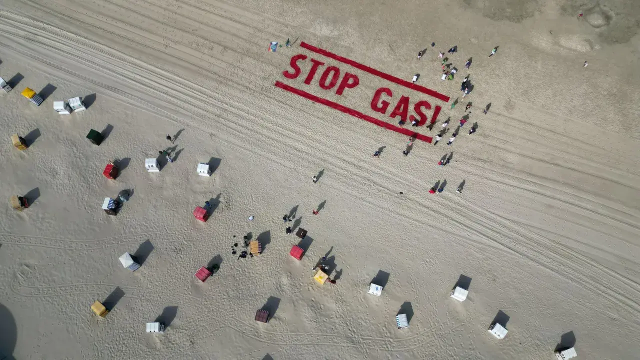 Menschen bilden auf einem Strand "STOP GAS!" als Zeichen für Deutschland klimaneutral. Viele Strandkörbe sind zu sehen.