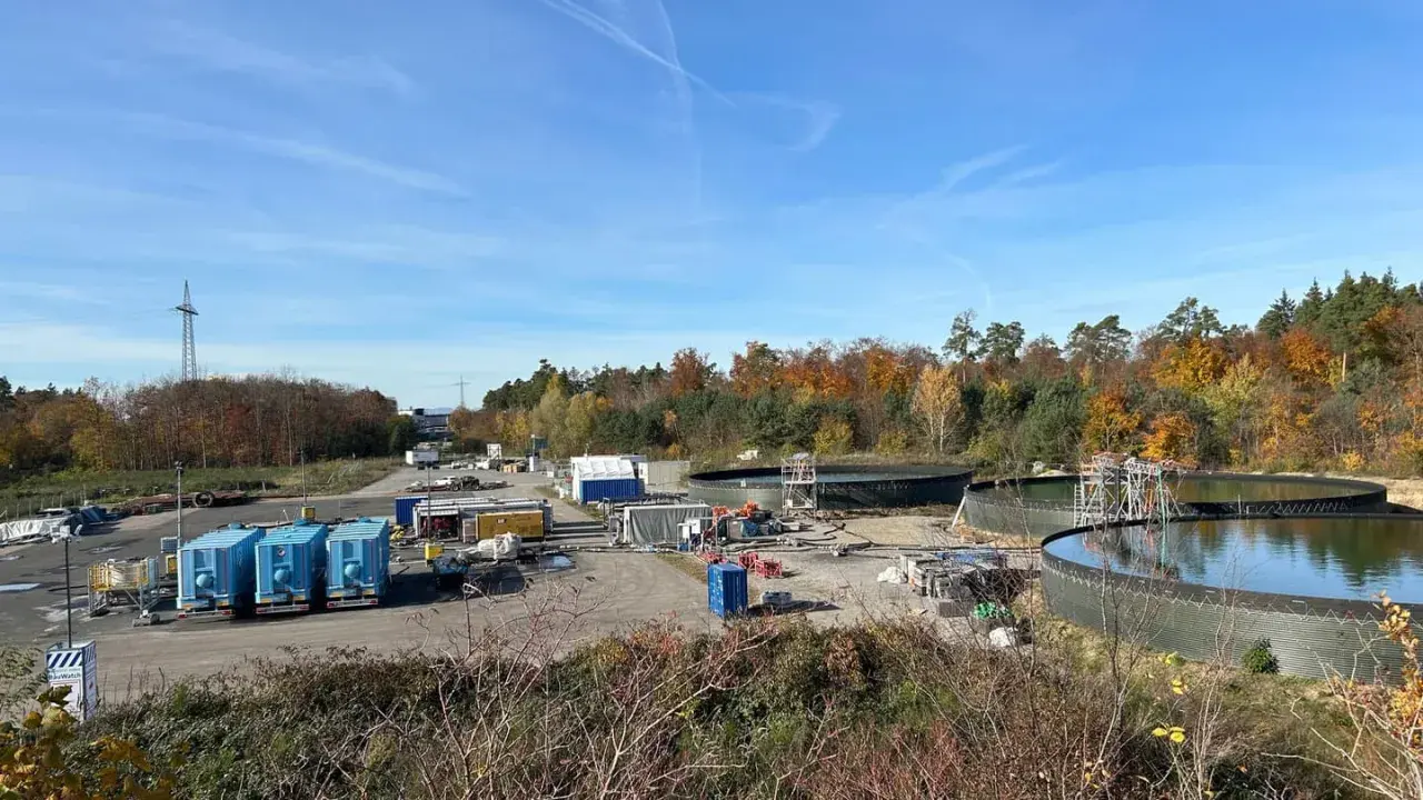 Baustelle mit großen Wasserbehältern und blauen Containern. Hier wird gezeigt, wie funktioniert geothermie mit Erdwärme.