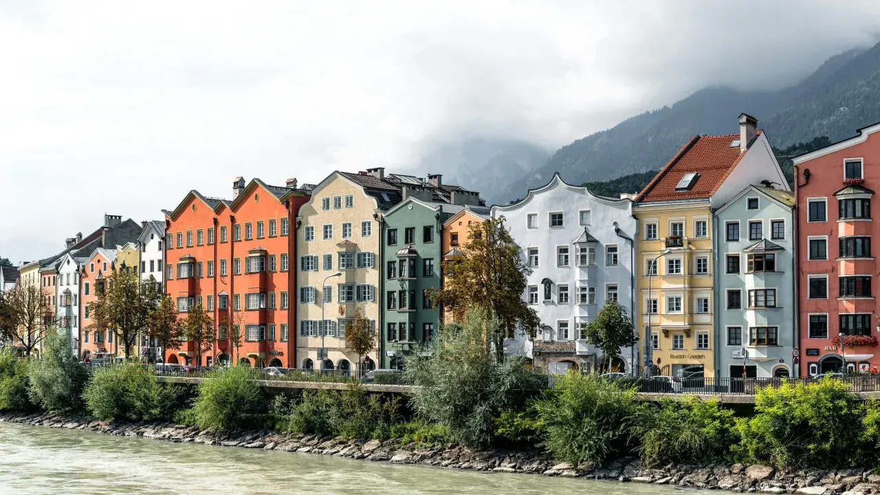 Bunte Häuserzeile am Flussufer, ein Beispiel dafür, was ein Ballungsraum ist: dicht bebaut, mit Bergen im Hintergrund.