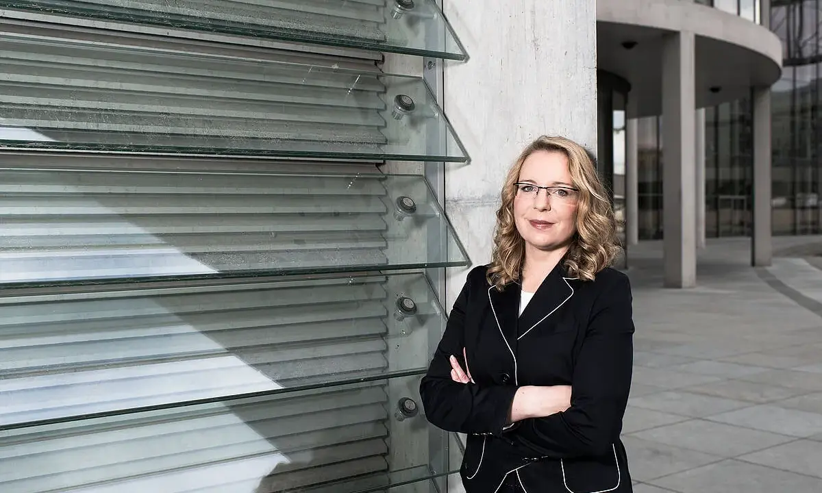 Frau Kemfert steht selbstbewusst vor einer modernen Glasfassade.
