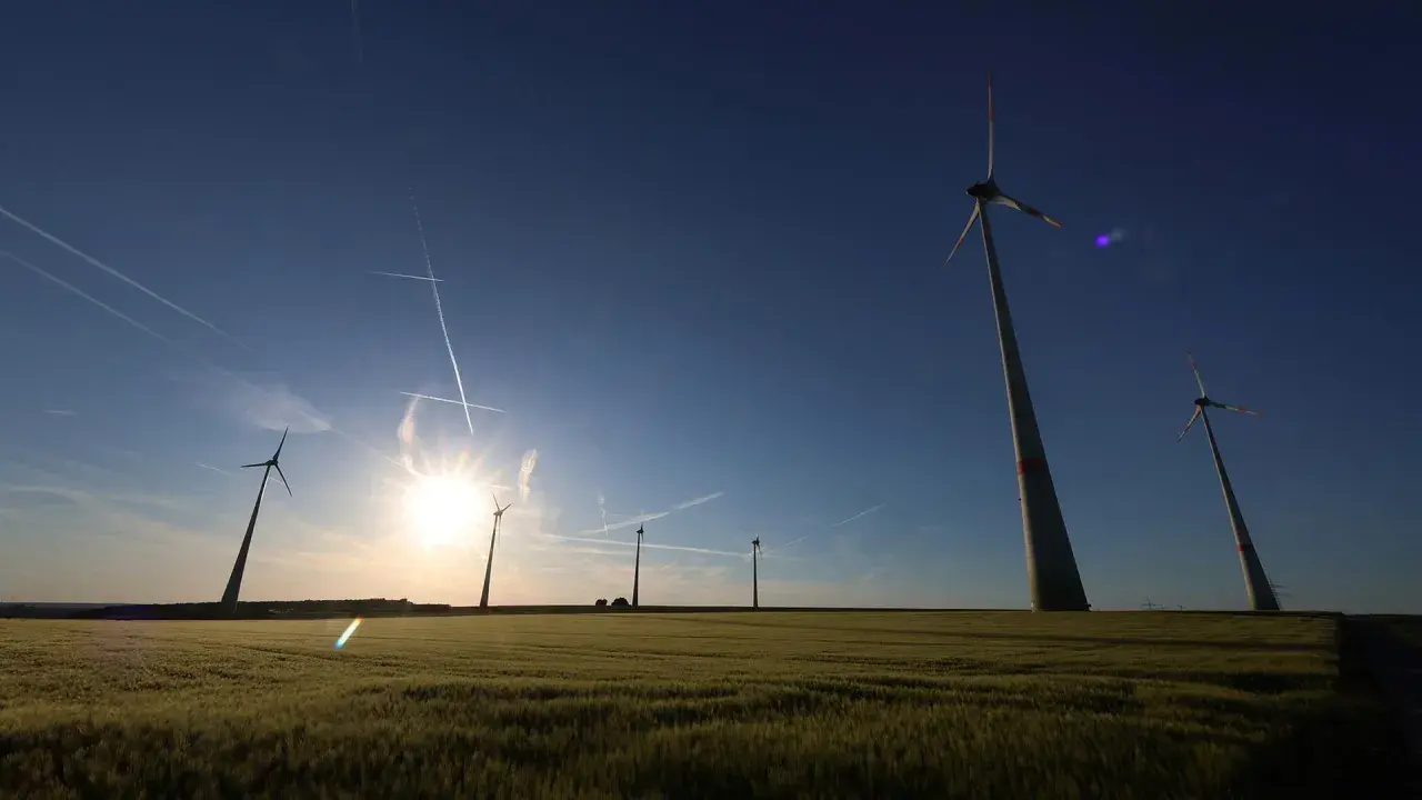 Windräder im Feld bei Sonnenuntergang, ein Symbol für den Windkraftausbau Deutschland. Kondensstreifen kreuzen den blauen Himmel.
