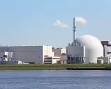 Großes Kernkraftwerk mit Kuppel und Kühlturm am Wasser.