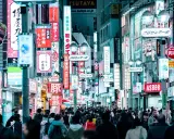 Eine belebte Straße mit vielen leuchtenden Neonschildern, die Geschäfte und Restaurants bewerben. Dies ist ein typisches Beispiel für einen urbanen Raum, voller Leben und Aktivität.