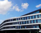 Modernes Gebäude des Fraunhofer IEE mit geschwungener Fassade und vielen Fenstern unter blauem Himmel mit Wolken.