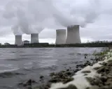 Kühltürme eines Atomkraftwerks mit Dampfschwaden über einem Flussufer.