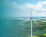 Windkraftanlage im Vordergrund, die sich dreht. Im Hintergrund eine Landschaft mit weiteren Anlagen, die die Amortisation der Windkraftanlage symbolisieren.