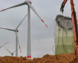Abrissbagger demontiert eine Windkraftanlage. Im Hintergrund stehen noch weitere Windräder, die ihre lange Laufzeit hinter sich haben.