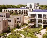 Moderne Gebäude mit Gründächern und Solaranlagen, umgeben von üppiger Vegetation. Ein Beispiel für nachhaltige Quartiersentwicklung.