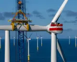 Bau eines Offshore-Windparks für die **Energie Niederlande**. Ein Kran hebt ein Rotorblatt einer riesigen Windkraftanlage im Meer.