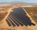 Große Solaranlage in Spanien, die die "Sonnensteuer" umgeht und saubere Energie liefert. Im Hintergrund Windräder und eine Stadt.