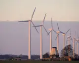 Windräder im Abendlicht, ein Traktor mit Anhänger und ein alter Mühlenbau symbolisieren die Direktvermarktung von Windstrom in ländlicher Idylle.