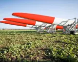 Drei Rotorblätter für Windkraftanlagen liegen auf einem Feld. Sie sind rot-weiß gestreift und warten auf ihren Einsatz nach dem EEG.