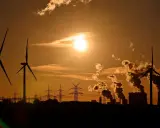 Silhouetten von Windrädern und rauchenden Industrieanlagen im Sonnenuntergang. Ein Bild, das zum Nachdenken über Stromkosten Norwegen vs. Deutschland anregt.
