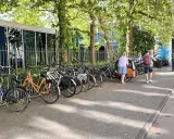Viele Fahrräder stehen am Straßenrand, ein Mann mit Kind auf dem Arm und eine Frau mit Lastenrad gehen vorbei. Eine echte Stadt der kurzen Wege.