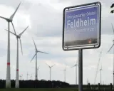 Schild "Energieautarker Ortsteil Feldheim, Stadt Treuenbrietzen" vor vielen Windrädern in Brandenburg.
