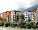 Bunte Häuserzeile am Flussufer, ein Beispiel dafür, was ein Ballungsraum ist: dicht bebaut, mit Bergen im Hintergrund.