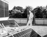 Mann mit Tablet inspiziert Solarmodule auf einem Dach. Der PV-Zubau in Deutschland schreitet voran.