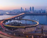 Verkehrsfluss in Seoul bei Nacht, mit Lichtern, die sich auf den Autobahnauffahrten und der Skyline der Stadt spiegeln.