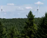 Zwei Windräder ragen über einen dichten Wald. Ein Onshore-Windpark in Deutschland, der saubere Energie erzeugt.