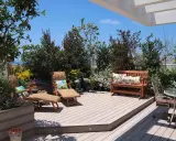 Ein idyllischer **garten auf dem dach** mit Holzdeck, Liegestühlen, Bank und üppiger Bepflanzung.