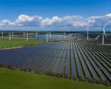 Großes Feld mit Windkraftanlagen und Photovoltaik-Modulen unter blauem Himmel mit Wolken.