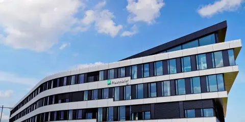 Modernes Gebäude des Fraunhofer IEE mit geschwungener Fassade und vielen Fenstern unter blauem Himmel mit Wolken.