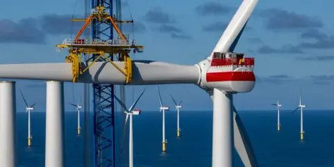 Bau eines Offshore-Windparks für die **Energie Niederlande**. Ein Kran hebt ein Rotorblatt einer riesigen Windkraftanlage im Meer.