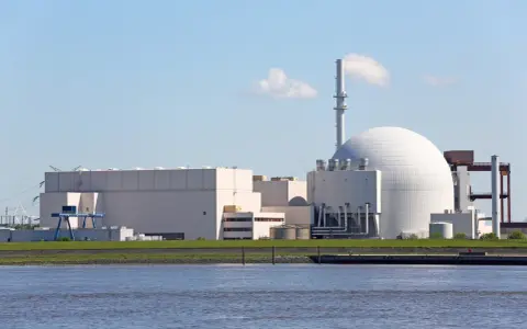 Großes Kernkraftwerk mit Kuppel und Kühlturm am Wasser.