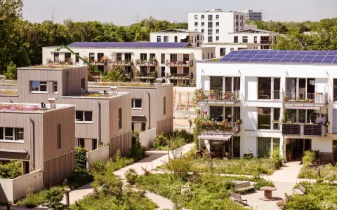 Moderne Gebäude mit Gründächern und Solaranlagen, umgeben von üppiger Vegetation. Ein Beispiel für nachhaltige Quartiersentwicklung.