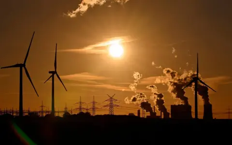 Silhouetten von Windrädern und rauchenden Industrieanlagen im Sonnenuntergang. Ein Bild, das zum Nachdenken über Stromkosten Norwegen vs. Deutschland anregt.