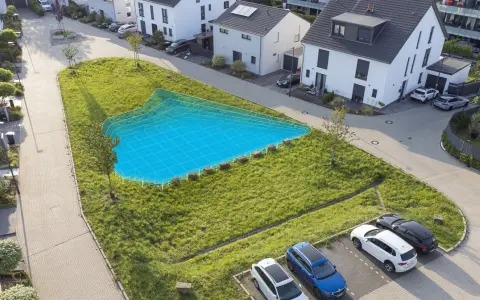 Eine blaue Fläche markiert eine geplante Mulde/Rigole in einem grünen Hang neben modernen Häusern und geparkten Autos.