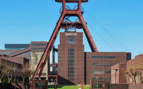 Industrielles Erbe mit rotem Förderturm und Backsteingebäuden. Die Zeche Zollverein strahlt eine starke, urbane Energie aus.
