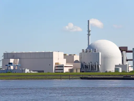 Großes Kernkraftwerk mit Kuppel und Kühlturm am Wasser.
