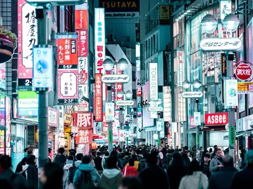 Eine belebte Straße mit vielen leuchtenden Neonschildern, die Geschäfte und Restaurants bewerben. Dies ist ein typisches Beispiel für einen urbanen Raum, voller Leben und Aktivität.