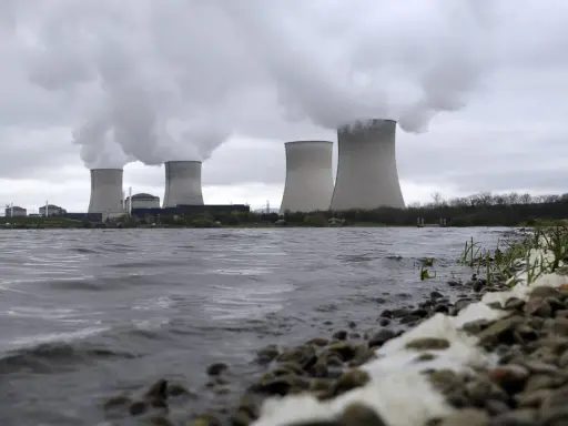 Kühltürme eines Atomkraftwerks mit Dampfschwaden über einem Flussufer.