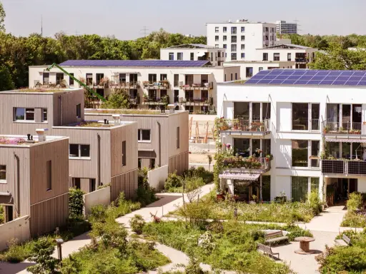 Moderne Gebäude mit Gründächern und Solaranlagen, umgeben von üppiger Vegetation. Ein Beispiel für nachhaltige Quartiersentwicklung.