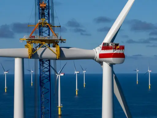 Bau eines Offshore-Windparks für die **Energie Niederlande**. Ein Kran hebt ein Rotorblatt einer riesigen Windkraftanlage im Meer.