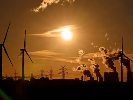 Silhouetten von Windrädern und rauchenden Industrieanlagen im Sonnenuntergang. Ein Bild, das zum Nachdenken über Stromkosten Norwegen vs. Deutschland anregt.