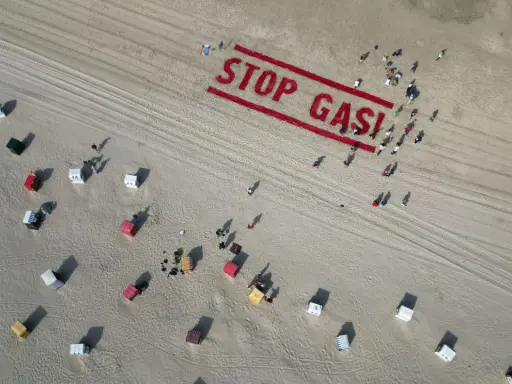 Menschen bilden auf einem Strand "STOP GAS!" als Zeichen für Deutschland klimaneutral. Viele Strandkörbe sind zu sehen.